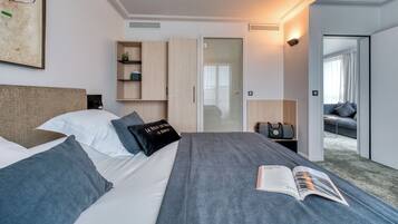 Une chambre d’hôtel moderne, dotée d’un grand lit, d’une table de chevet, d’une lampe de lecture, d’une armoire et donnant sur la chambre voisine.