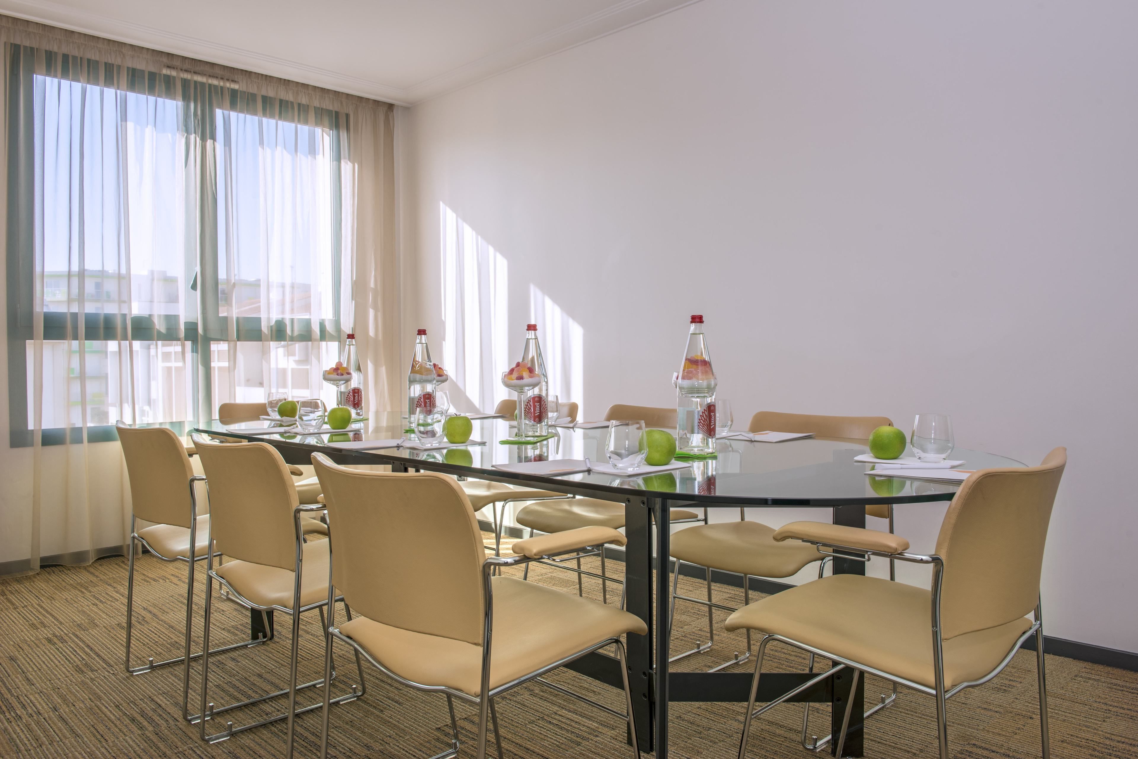 A conference room with a glass table, beige chairs, and a window with curtains.