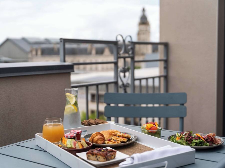 Una mesa en el balcón con alimentos para el desayuno, como cruasanes, muffins, una ensalada de frutas y una bebida.