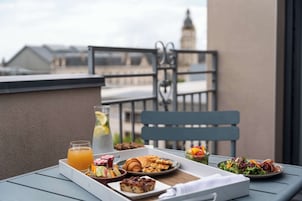 Una mesa en el balcón con alimentos para el desayuno, como cruasanes, muffins, una ensalada de frutas y una bebida.