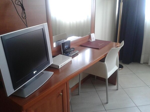 Habitación de hotel con un escritorio de madera, un televisor de pantalla plana, una computadora portátil, un teléfono y una silla.