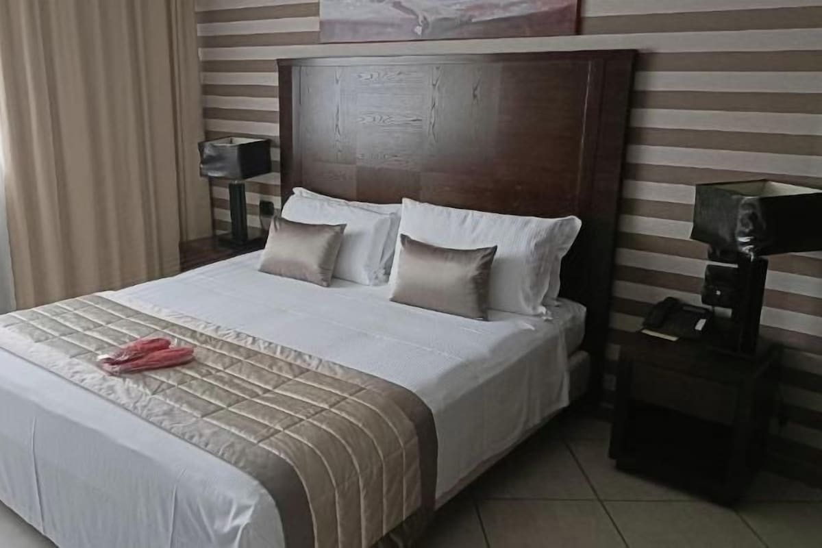 A hotel room with a large bed, a headboard, bedside tables, and a window with curtains.