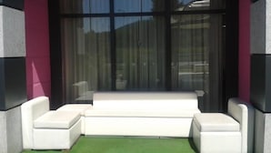 Un sofá blanco con piso de césped artificial verde, ubicado frente a un amplio ventanal con cortinas.