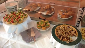 Un bufé con diversas opciones de comida, entre ellas pasteles, tartas y pizza.