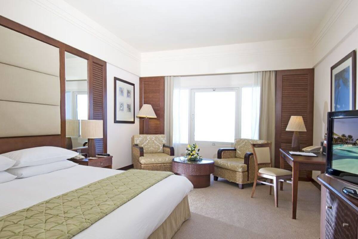 A hotel room with a large bed, two armchairs, a desk with a television, and a window with curtains.