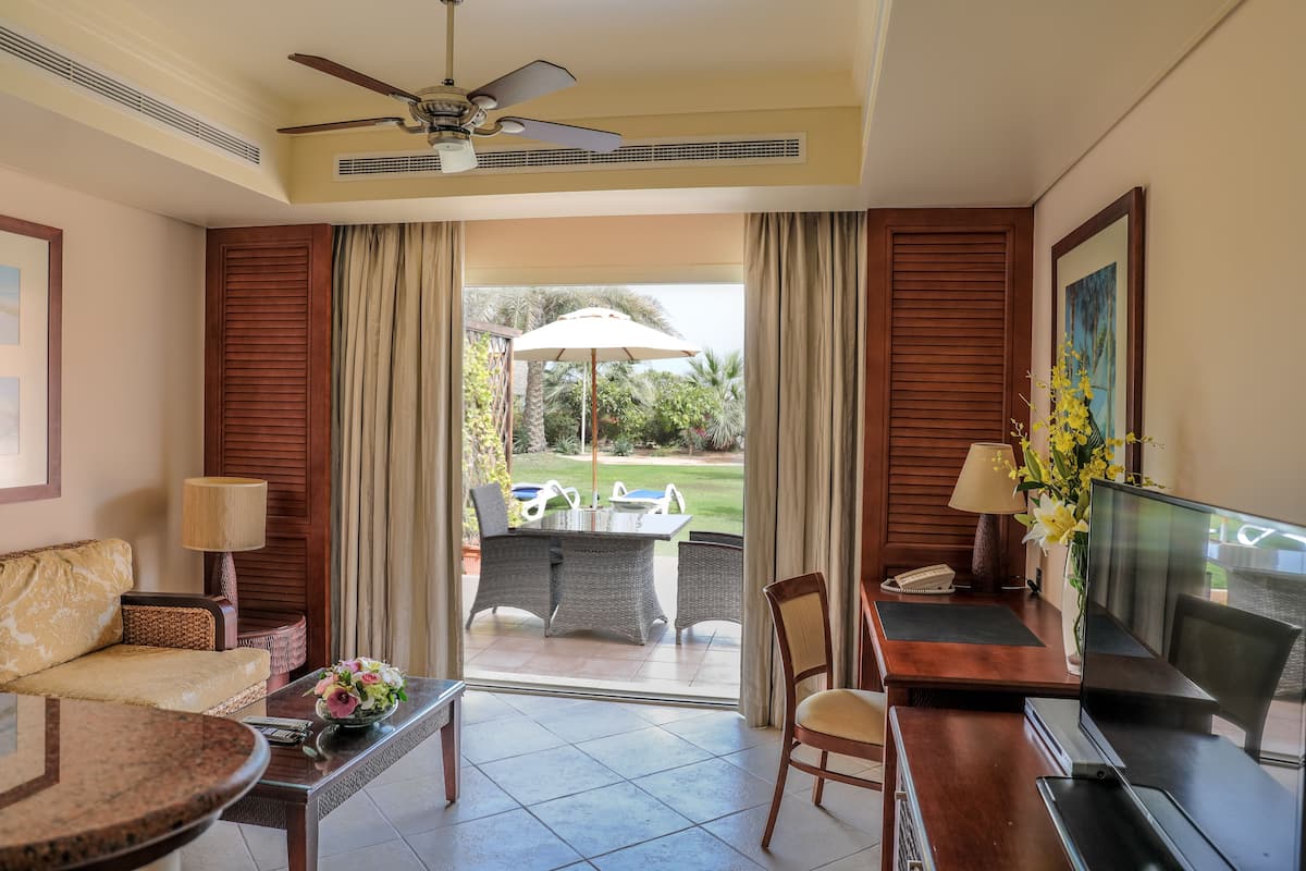 A hotel room with a balcony, a dining table, a sofa, a TV, and a desk.