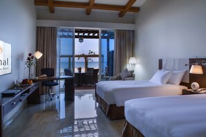 Een hotelkamer met twee bedden, een bureau en uitzicht op zee.
