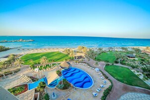 Resort com uma piscina grande, praia e palmeiras.