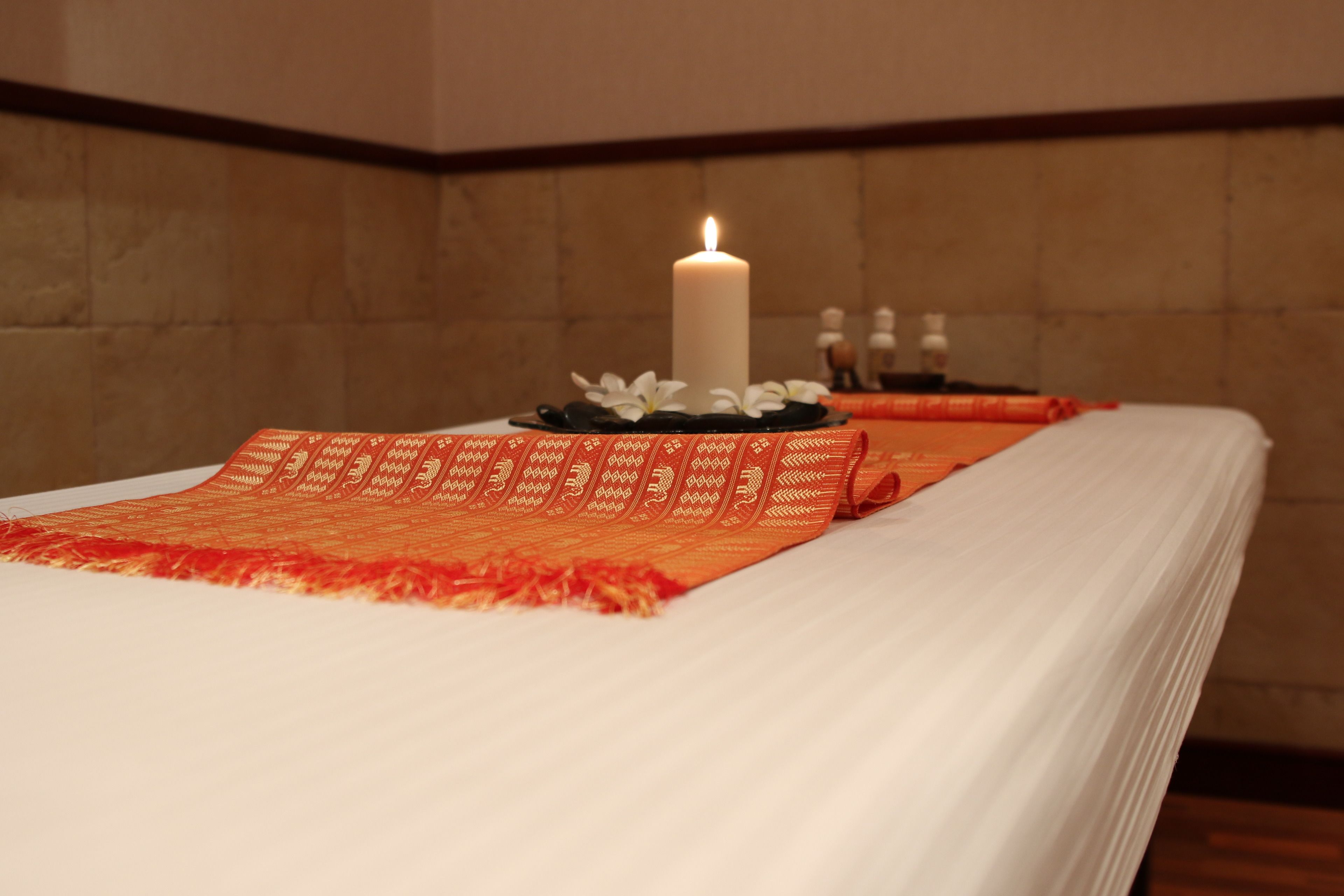 A spa room with a white bed, a lit candle, and a decorative orange and red patterned cloth.