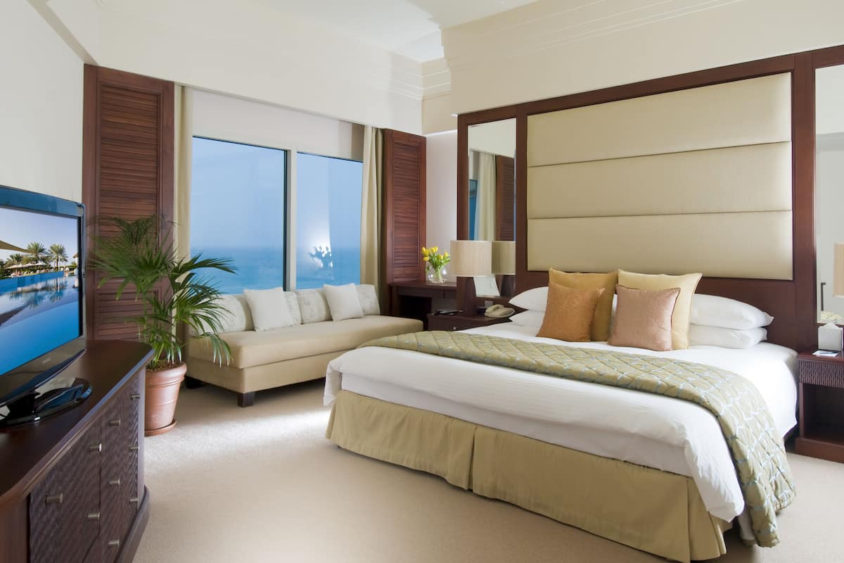 A hotel room with a large bed, a sofa, a television, a potted plant, and a view of the ocean.