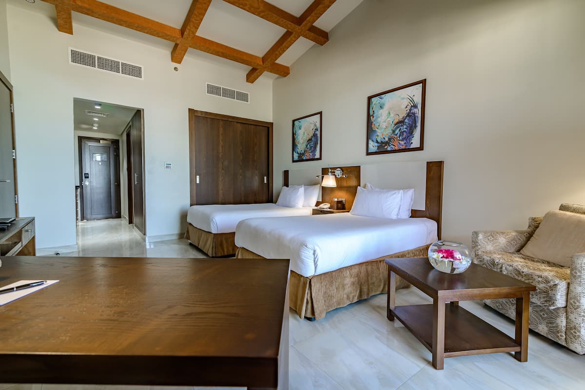 A hotel room with two beds, a sofa, a wooden table, and artwork on the walls.