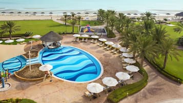 Relax by the resort's wave-patterned pool, surrounded by lounge chairs and umbrellas, with a children's play area nearby.