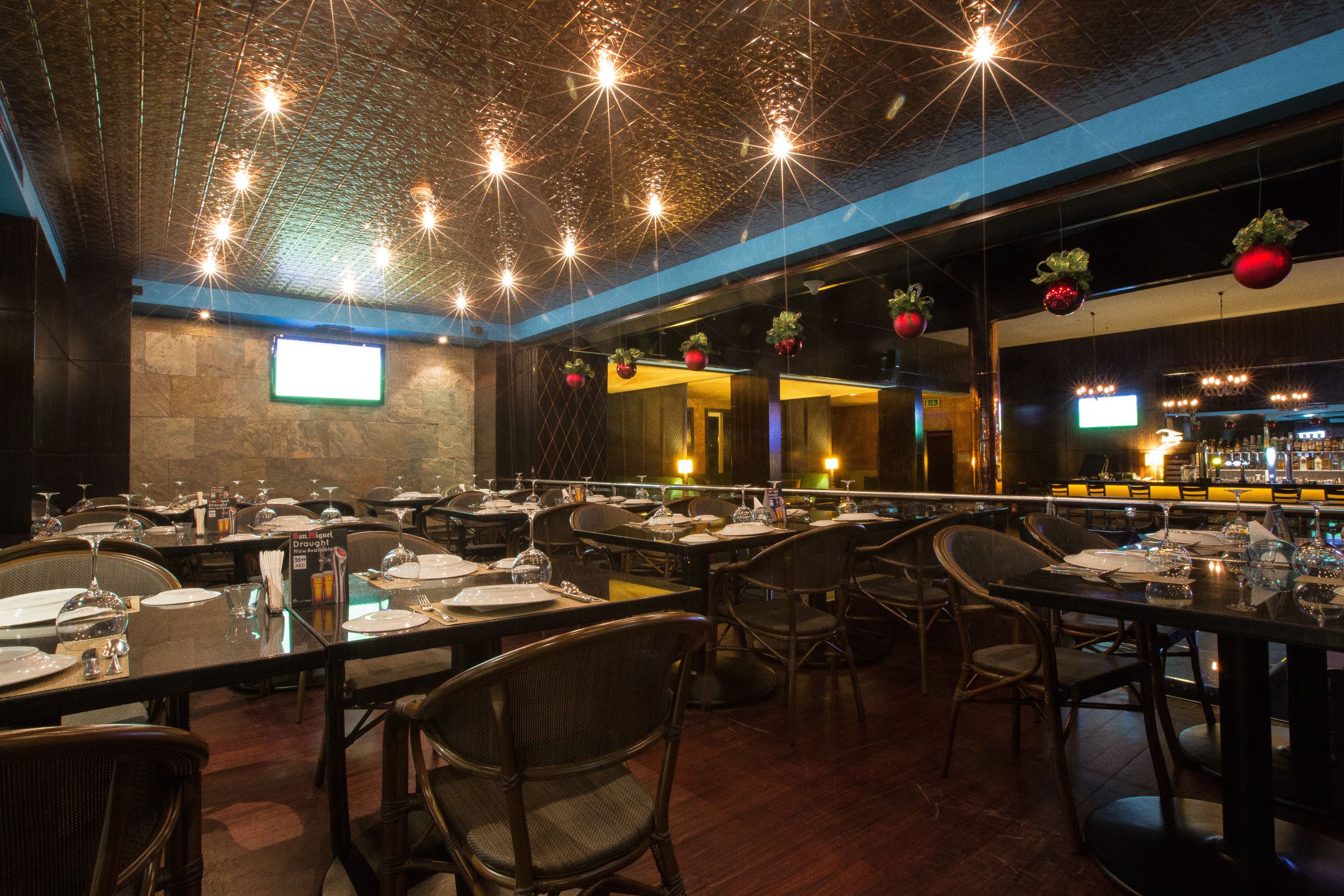 A restaurant with multiple tables set for dining, a bar area, and a projection screen on the wall.