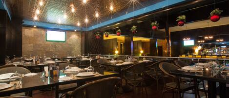 A restaurant with multiple tables set for dining, a bar area, and a projection screen on the wall.