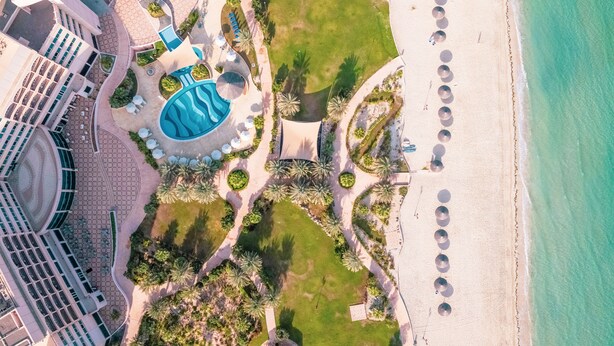 Vue aérienne d’un complexe hôtelier doté d’une piscine, d’une plage et d’un grand bâtiment à la forme circulaire.