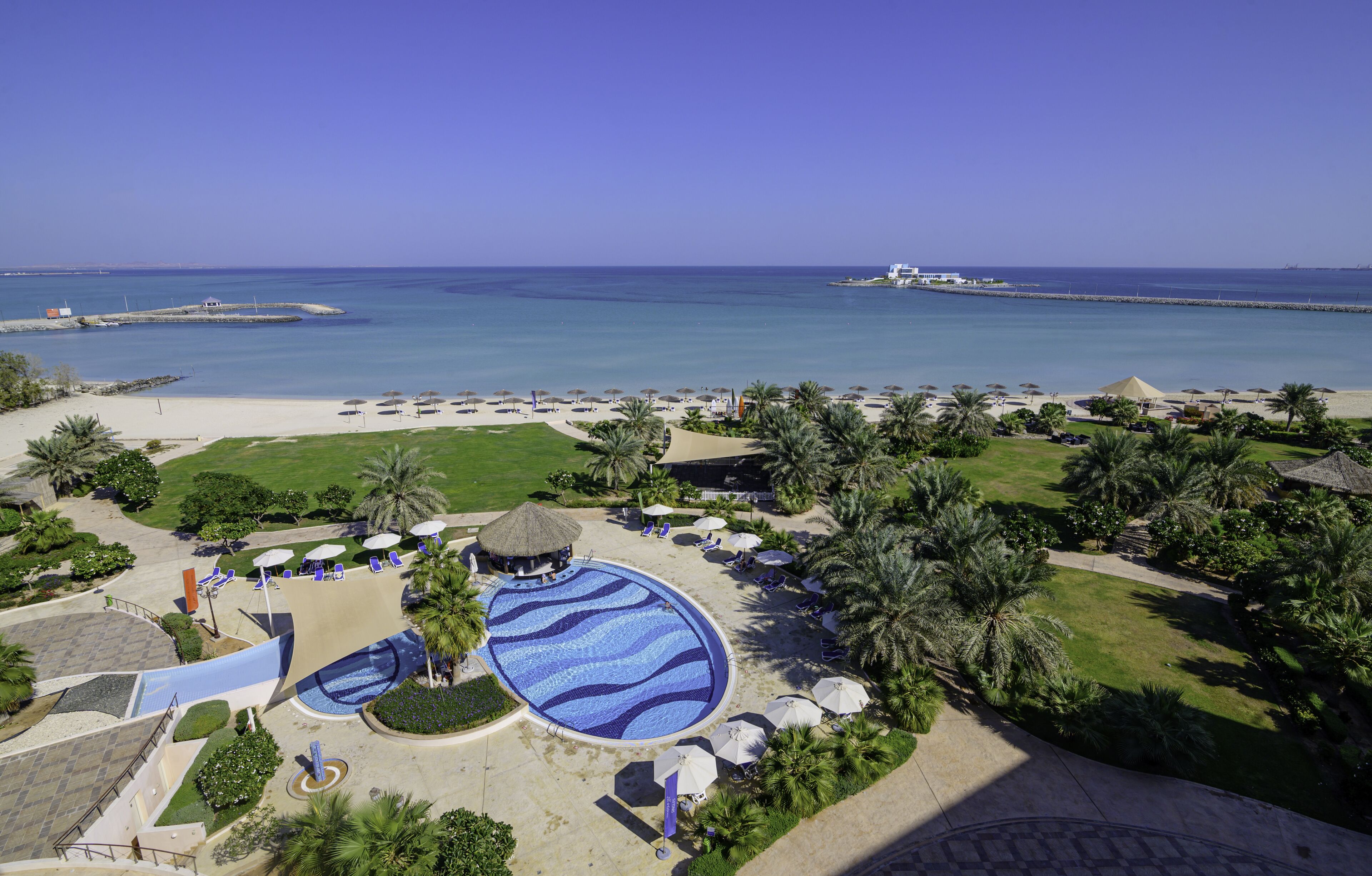 Lomakeskus, jossa on suuri uima-allas, ranta-alue ja palmuja.