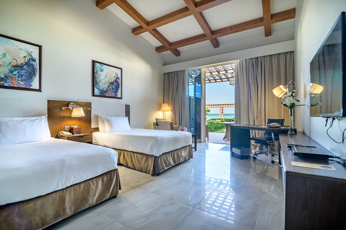 A hotel room with two beds, a desk, and a view of the outdoors.