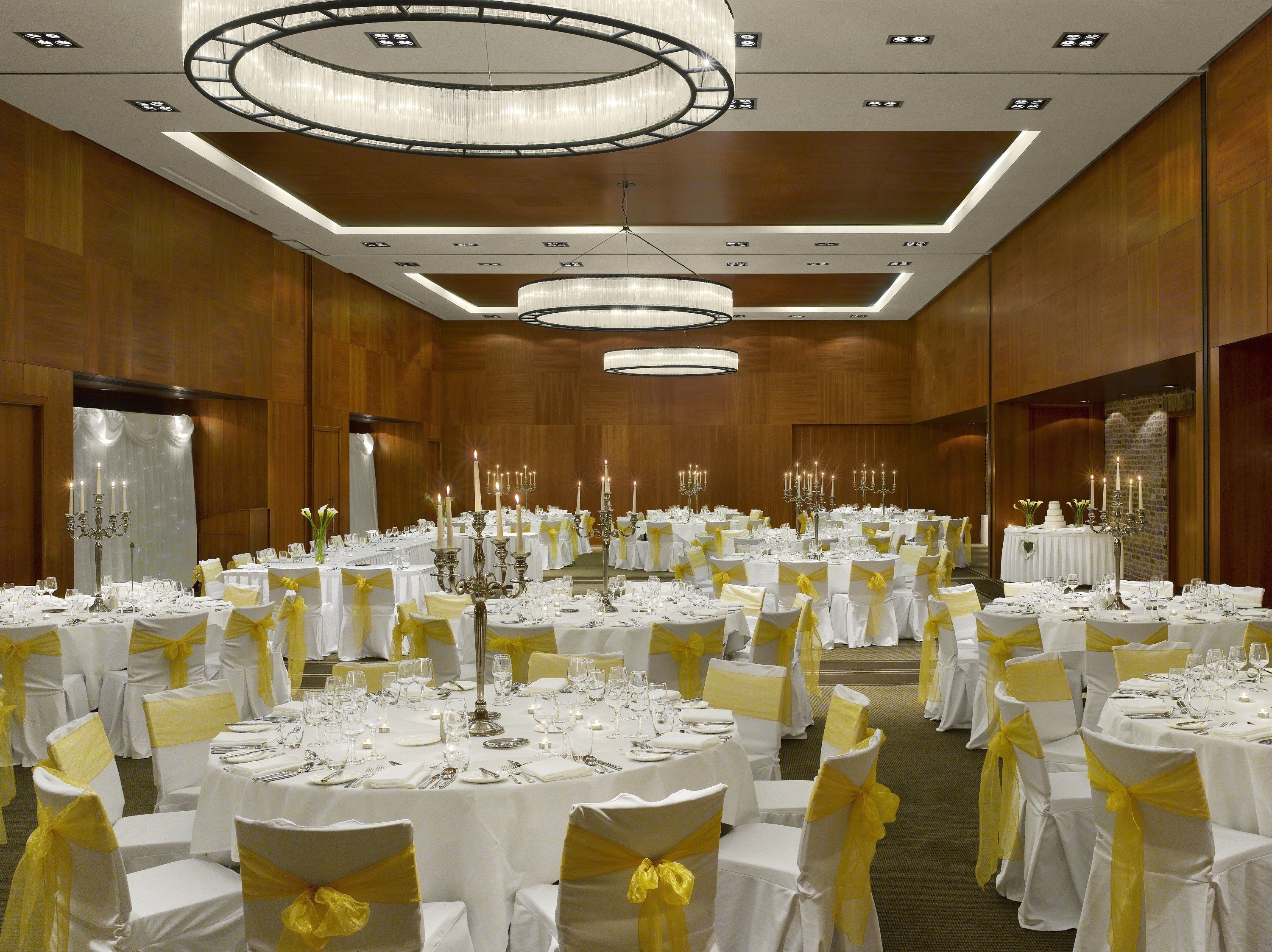 A banquet hall with round tables, white tablecloths, and yellow sashes on chairs.