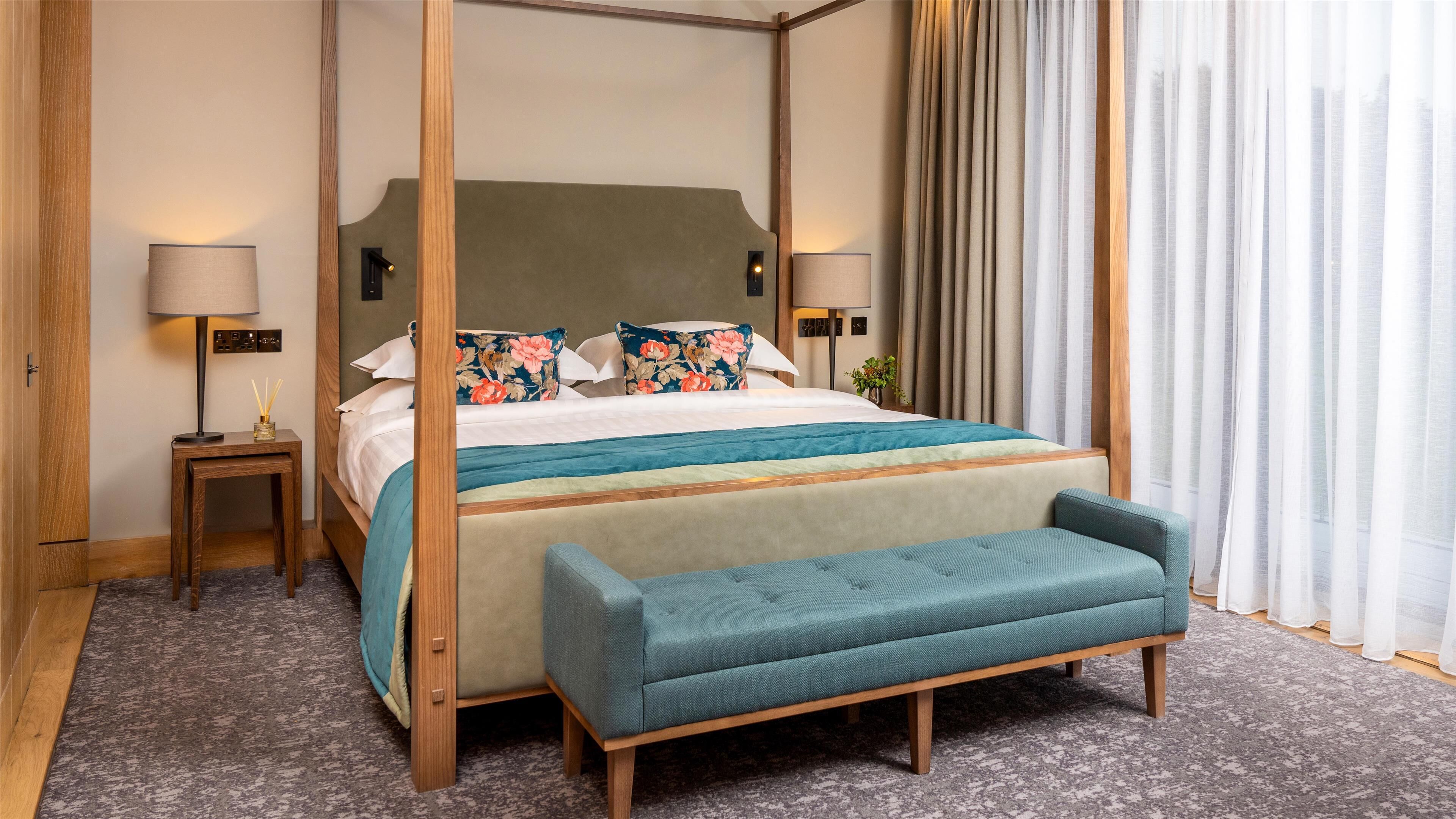 A four-poster bed with a floral pillow, bedside tables with lamps, and a bench at the foot of the bed.