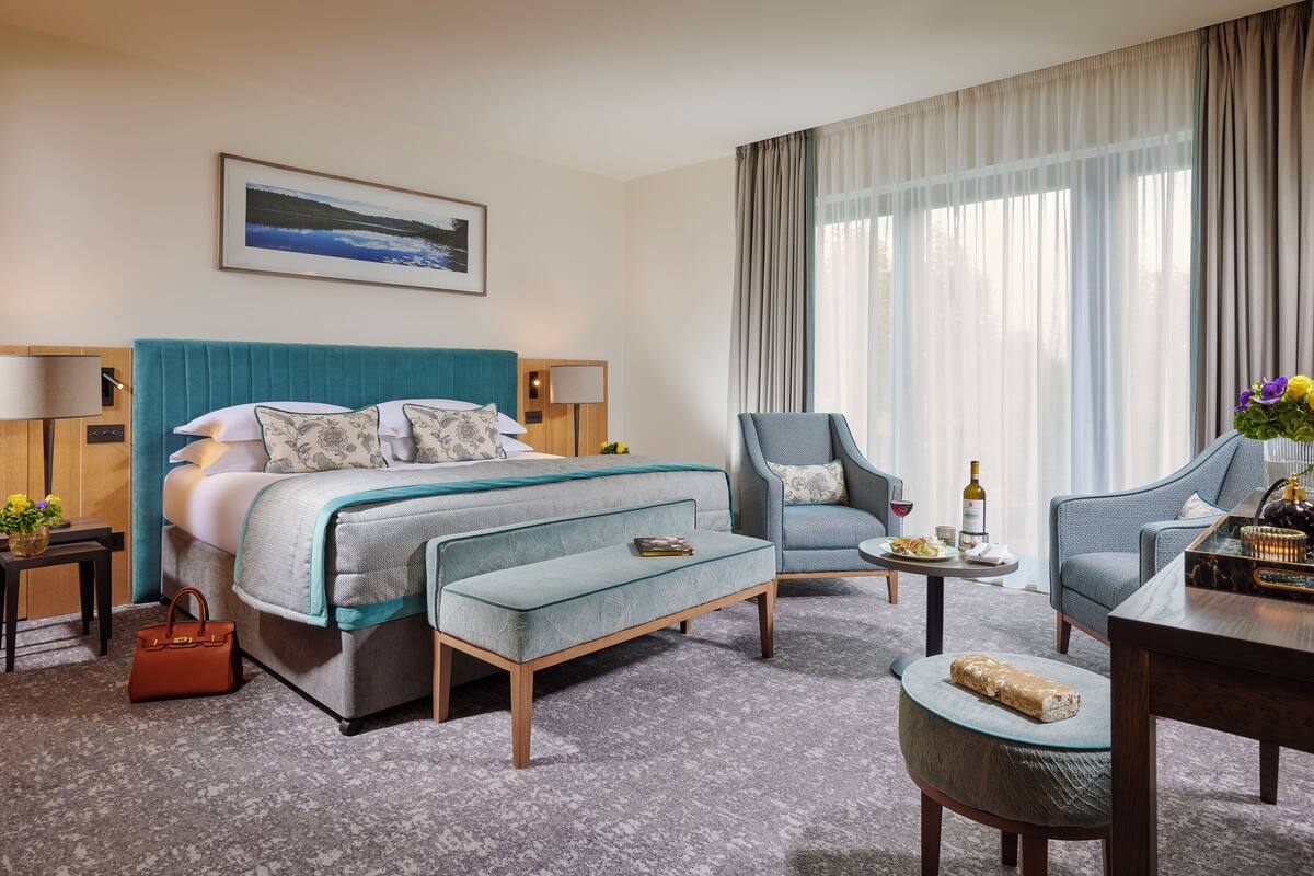 A hotel room with a bed, two armchairs, a small table, a coffee table, a sofa, a side table, and a window with curtains.