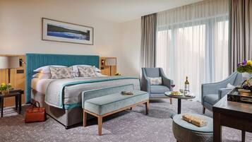 A hotel room with a bed, two armchairs, a small table, a coffee table, a sofa, a side table, and a window with curtains.