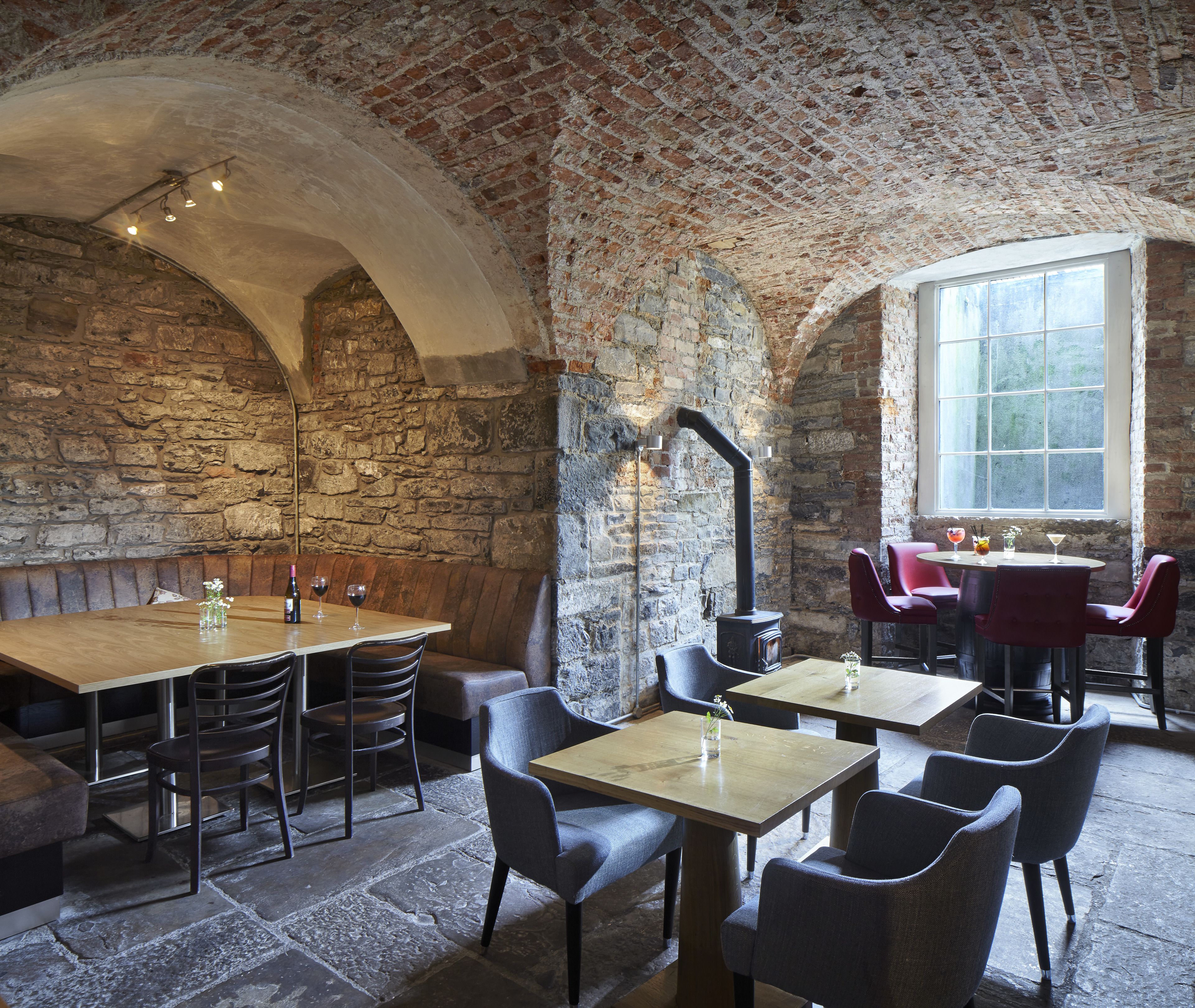 A rustic dining area with stone walls, wooden tables, and leather chairs.