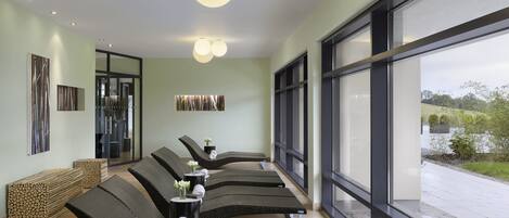 A modern spa area with reclining chairs, a large window offering a view of the outdoors, and a ceiling with recessed lighting.