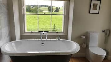 A bathroom with a freestanding bathtub, a toilet, and a window with a view of a green field.