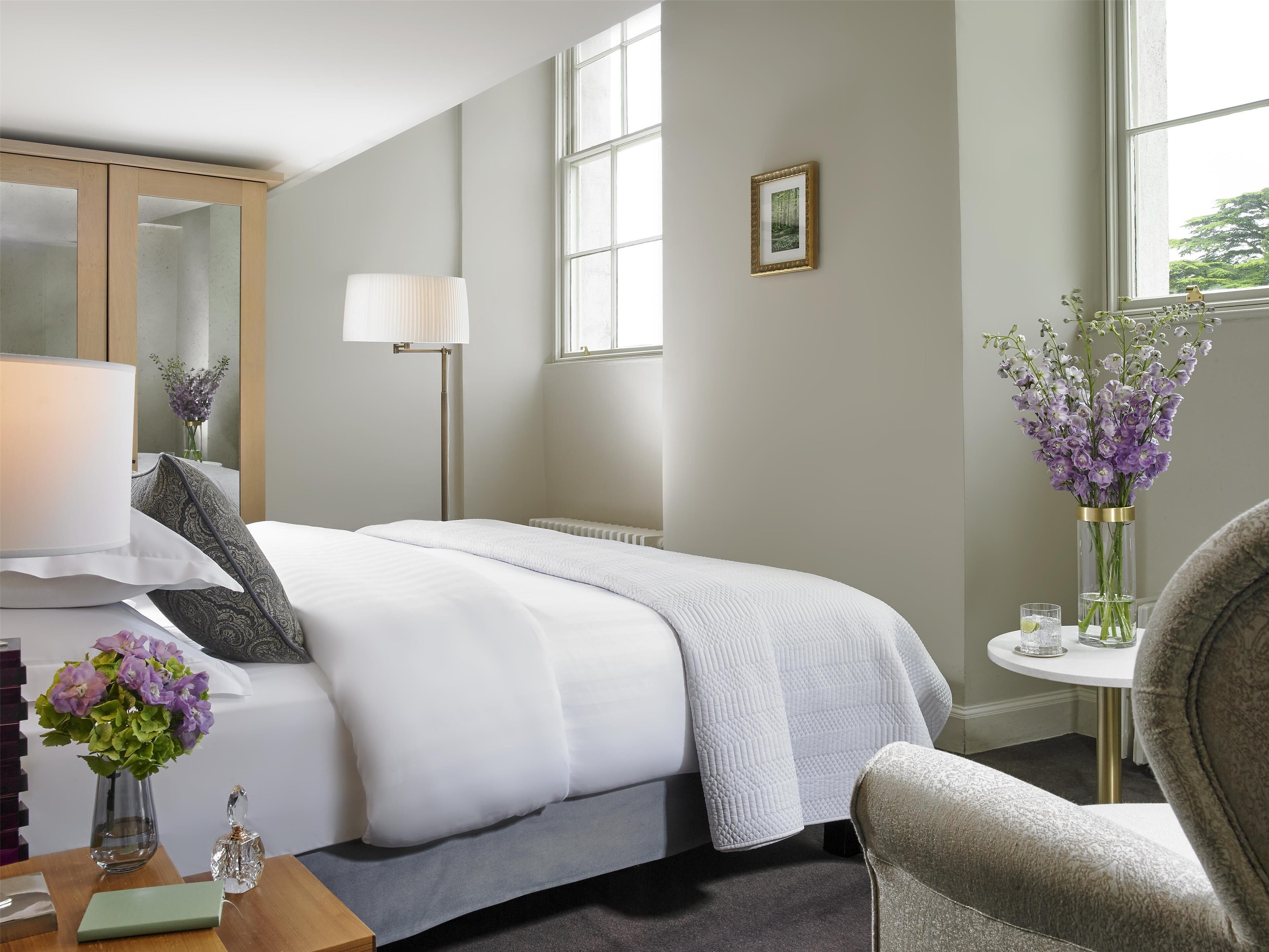 Una habitación de hotel con cama, mesita de noche, lámpara, flores y ventana.