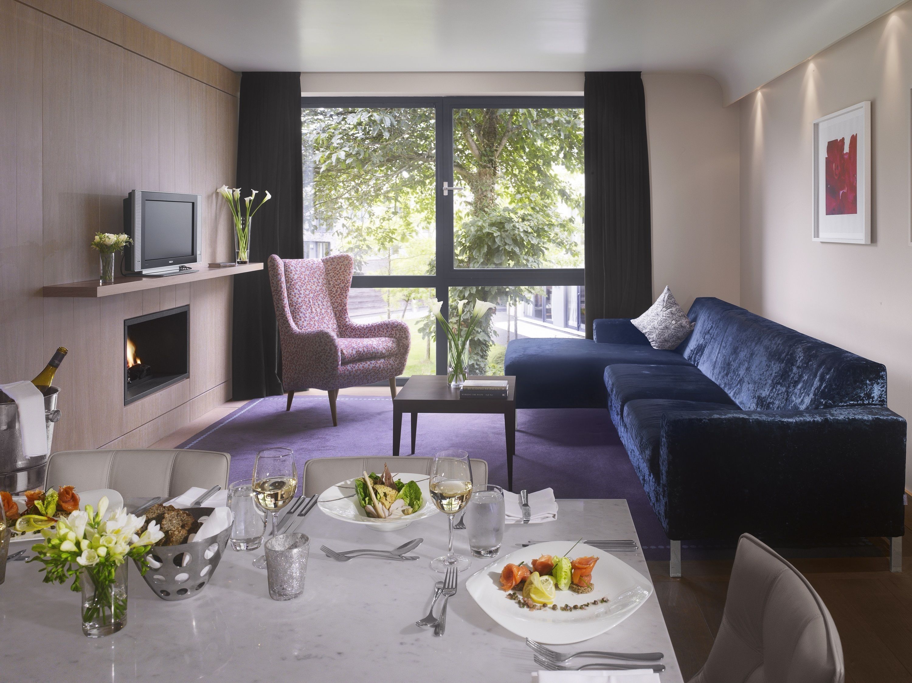 Una sala de estar moderna con chimenea, un sofá azul y un comedor listo para una comida.