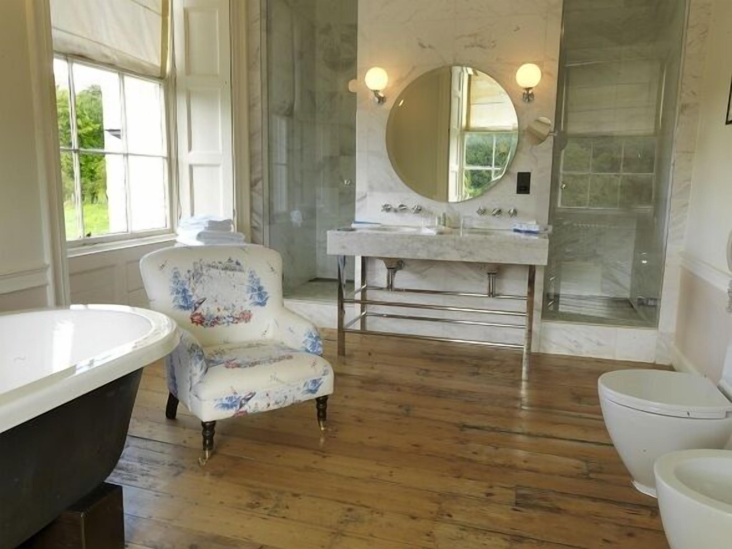 A bathroom with a freestanding bathtub, a round mirror above the sink, and a wooden floor.