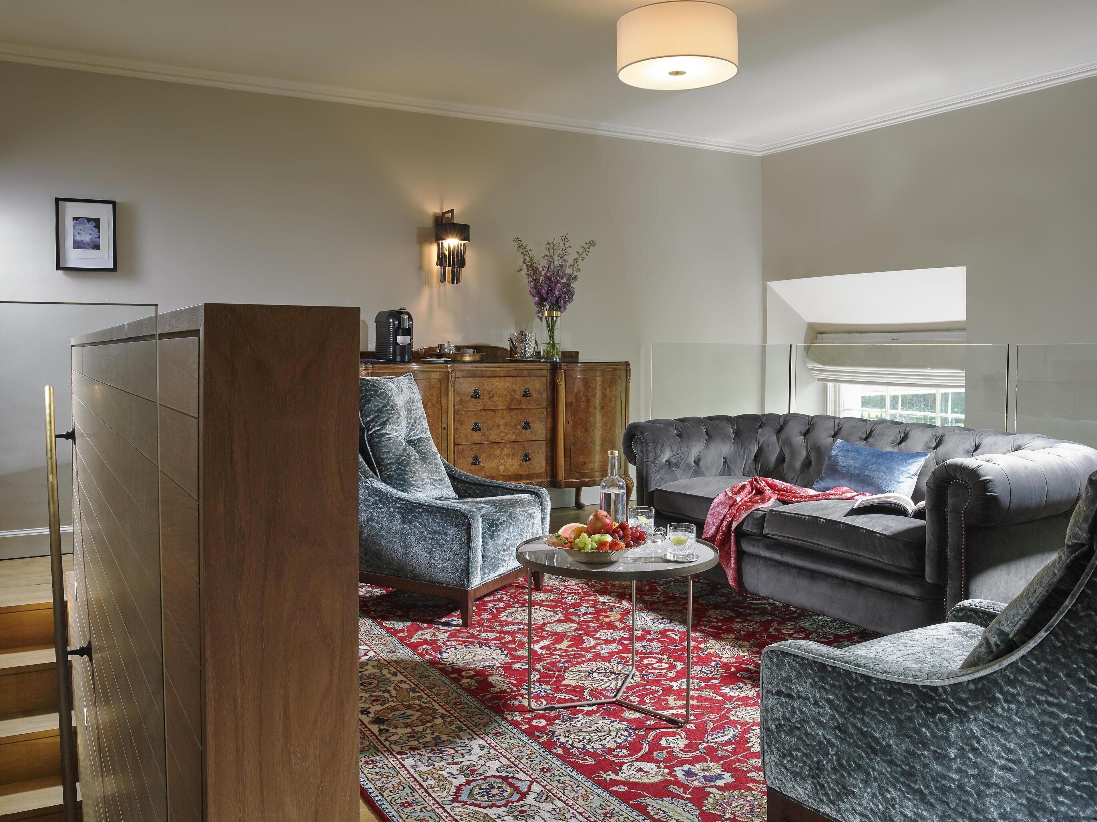 A living room with a grey sofa, a blue armchair, a wooden cabinet, and a red patterned rug.