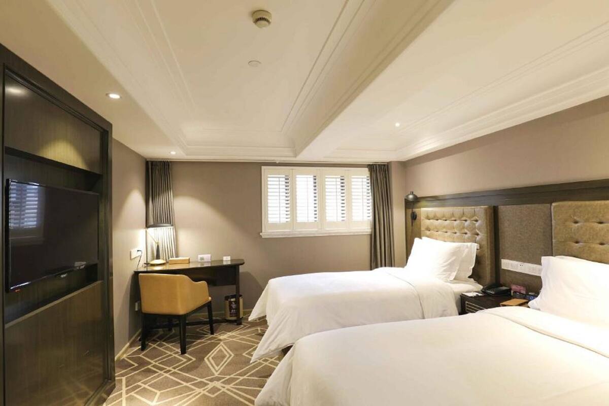 Habitación de hotel con dos camas, un escritorio, una silla, televisión y ventana con persianas.