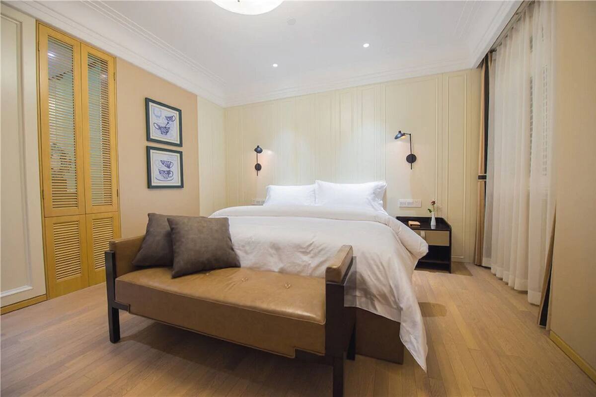 Un dormitorio con cama, sofá, mesita de noche y lámpara de pared.