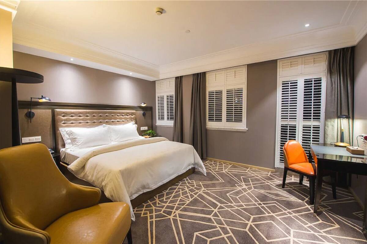 Una habitación de hotel con una cama grande, un escritorio con una silla y una alfombra estampada.