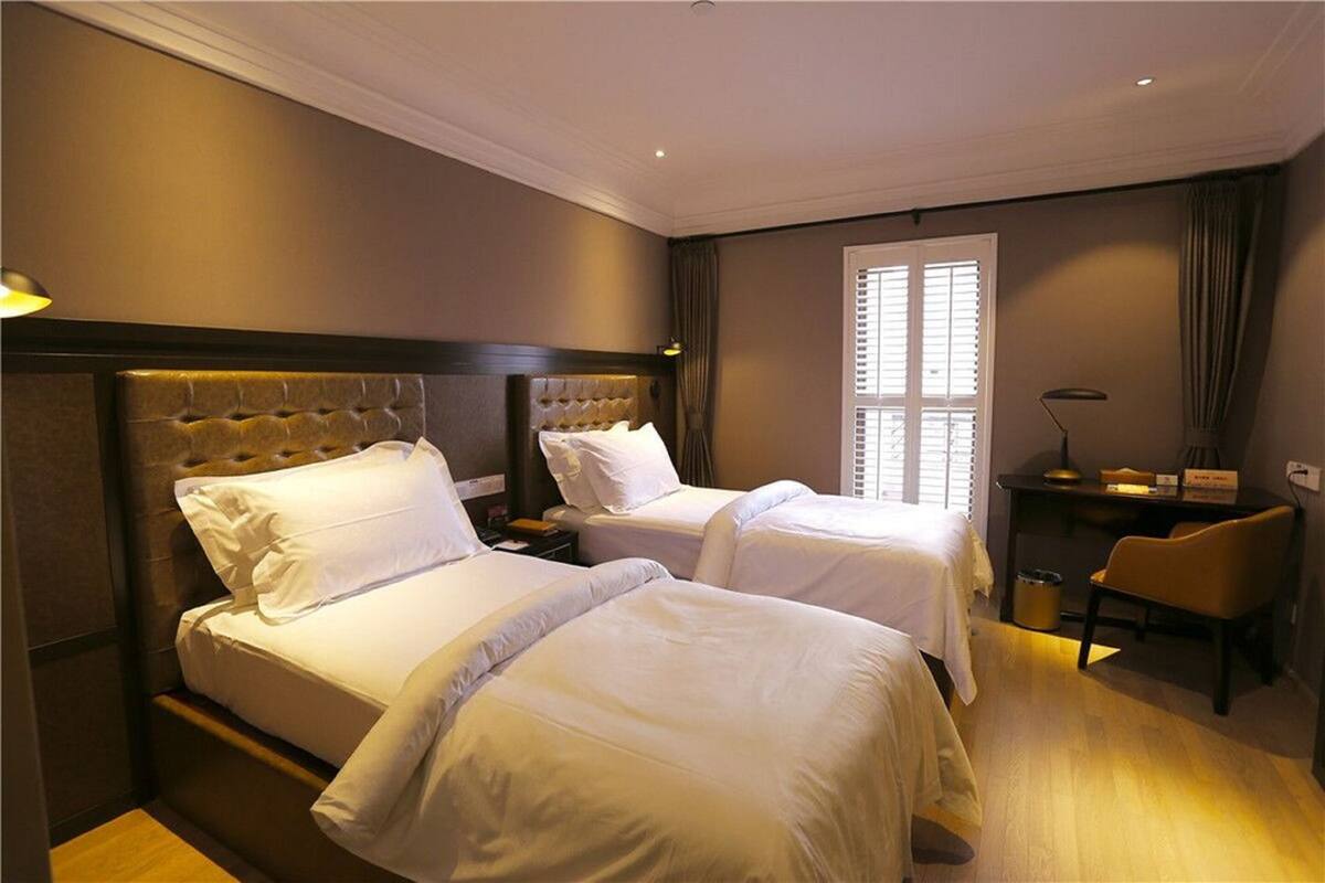 Una habitación de hotel con dos camas, un escritorio, una silla y una ventana con persianas.
