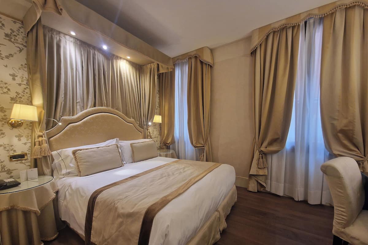 A hotel room with a large bed, two bedside tables, a chair, and curtains.