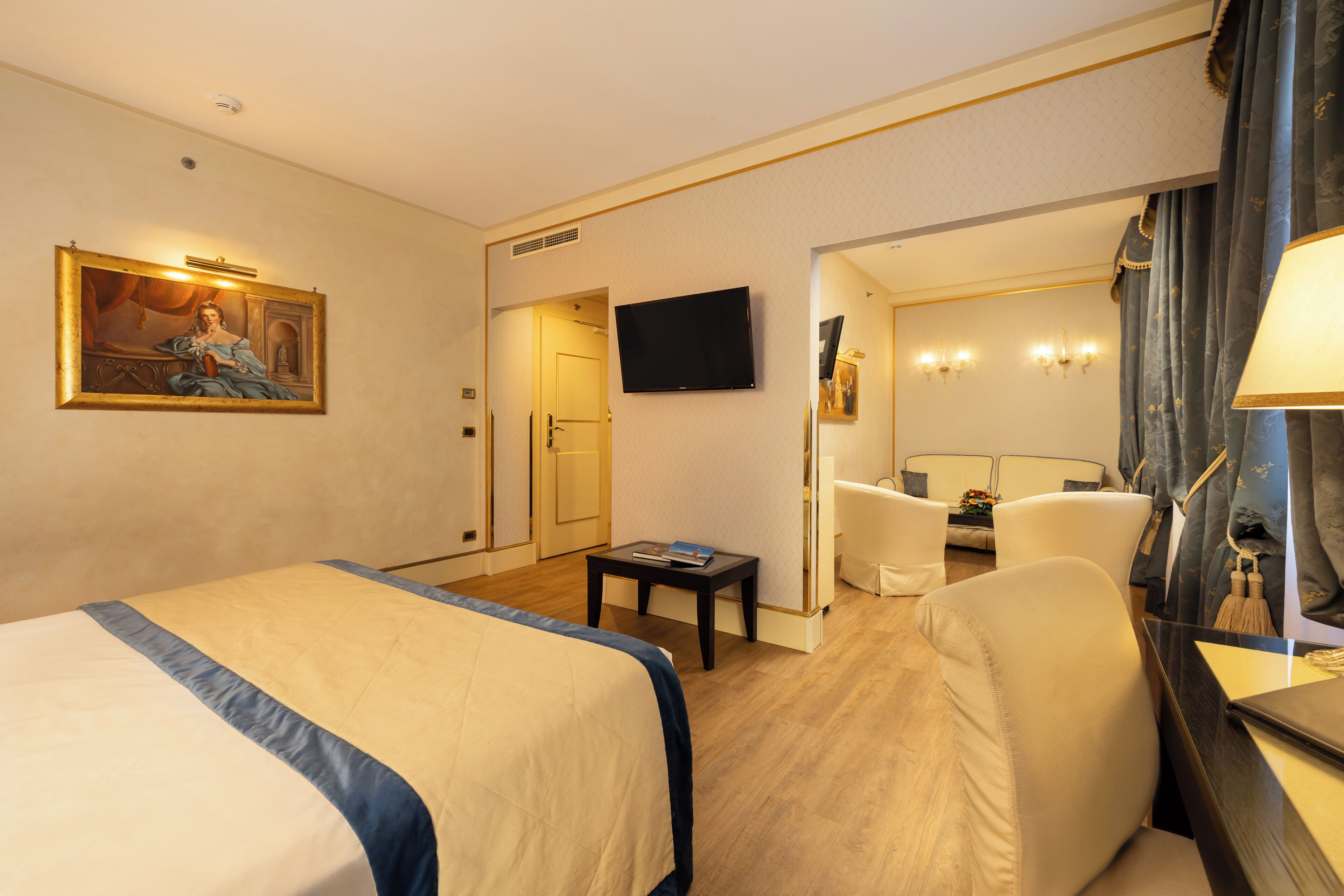 Hotellihuone, jossa on suuri sänky, työpöytä, tuoli, televisio ja taulu seinällä.