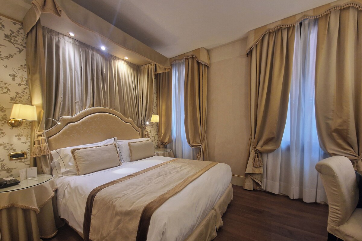 A hotel room with a large bed, two bedside tables, a chair, and curtains.
