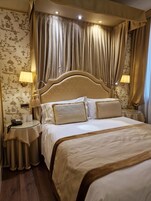 A hotel room with a large bed, two bedside tables, a wall-mounted lamp, and a curtain.