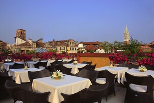 Un'area pranzo all'aperto con tavoli e sedie, circondata da edifici e da un campanile.