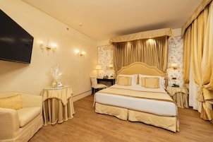 Habitación de hotel con una cama grande, dos mesitas de noche, un televisor y una zona de estar con sofá.