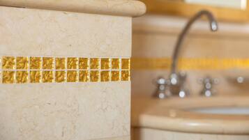 A bathroom with a marble wall, a gold-tiled accent strip, and a sink with a faucet.