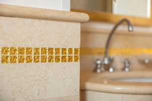 Un baño con pared de mármol, una franja decorativa de azulejos dorados y un lavamanos con grifo.