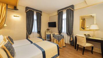 Camera d'albergo con due letti, una scrivania, una sedia, una TV e un comodino con una lampada.