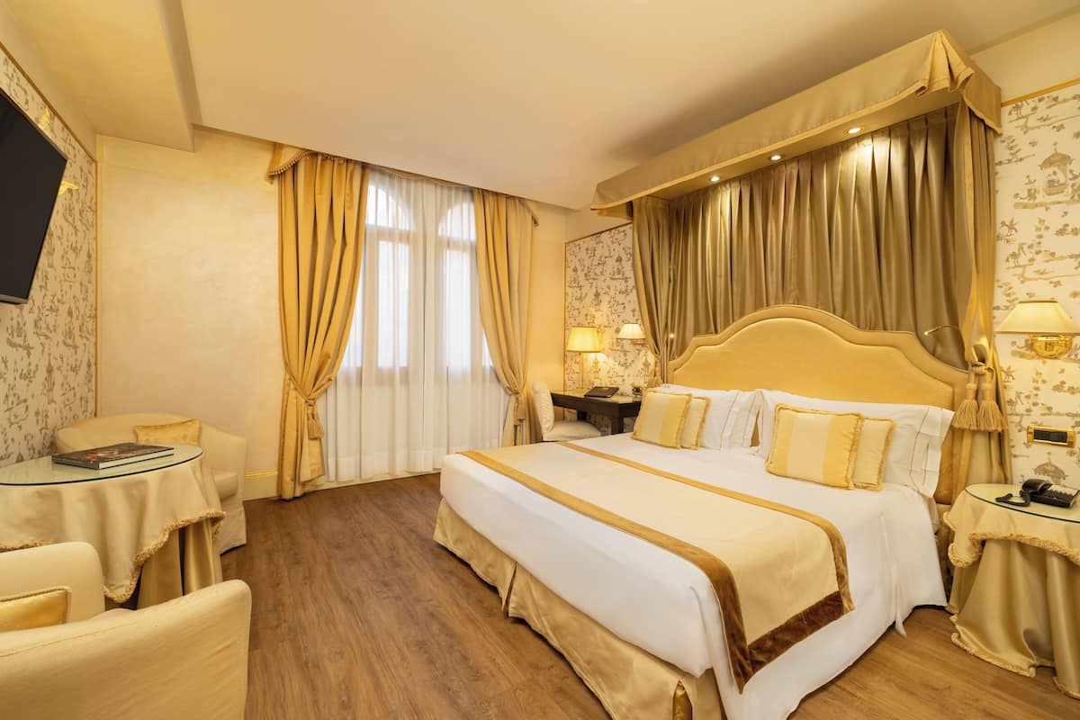 Habitación de hotel con una cama grande, un escritorio con silla, una mesita y un televisor.