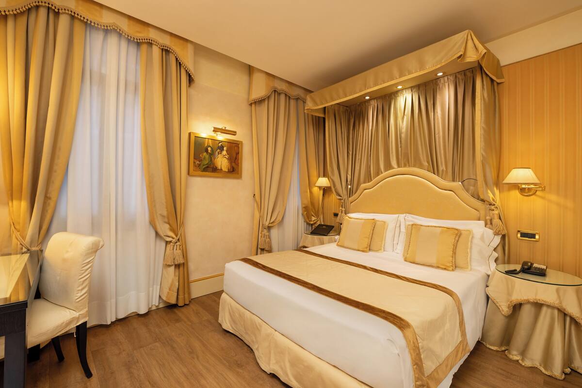 Una habitación de hotel con una cama grande, dos mesitas de noche, una silla y cortinas.