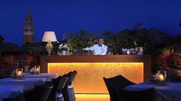 A bar area with a bartender, tables with candles, and a view of a tower in the background.