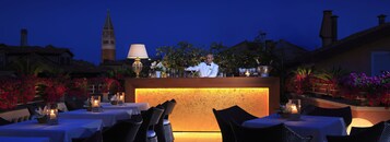 A bar area with a bartender, tables with candles, and a view of a tower in the background.