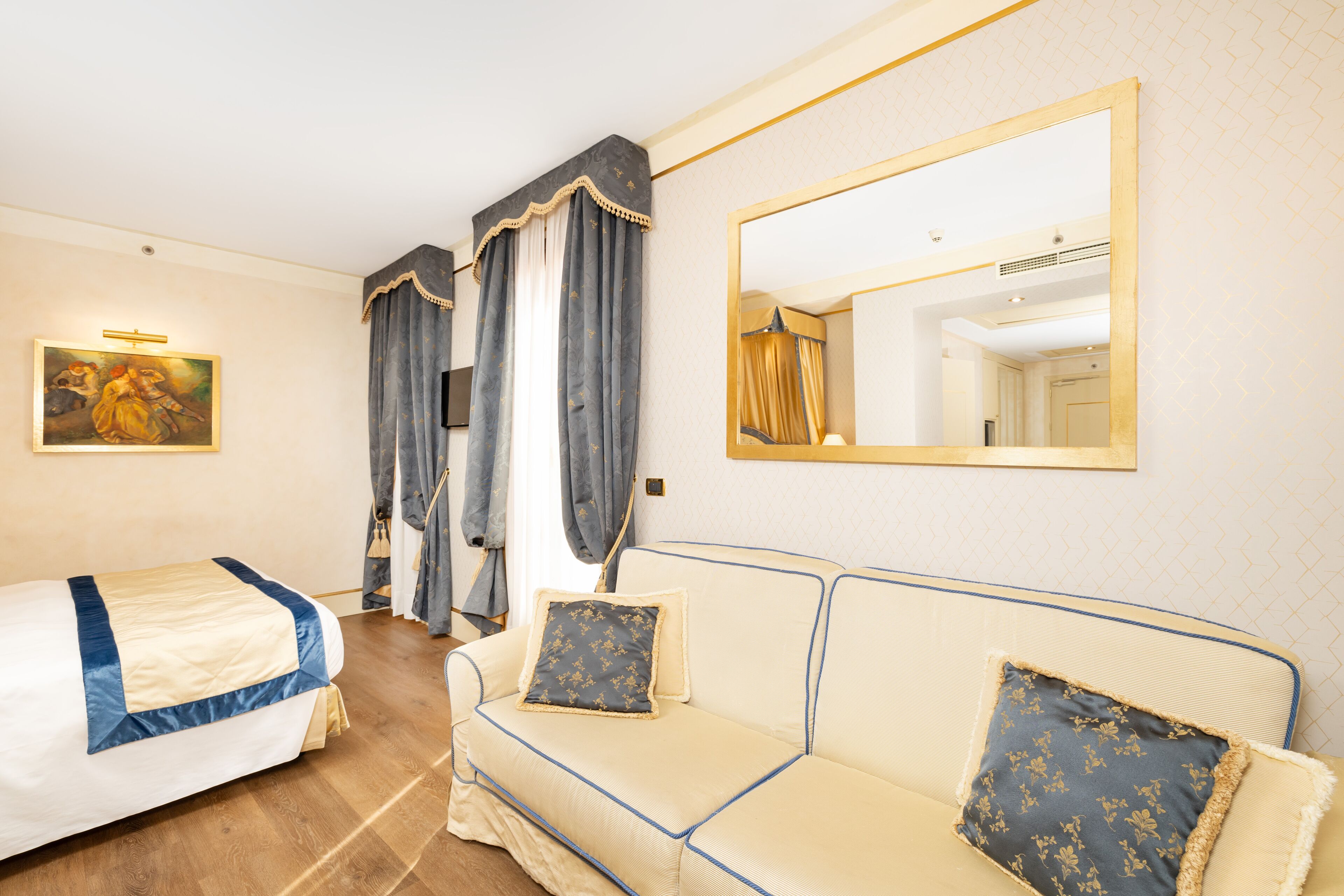 A hotel room with a bed, a sofa, a large mirror, and a painting on the wall.